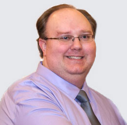 Photo of Eric Brockway, Lead Developer for Brukenet Web Development. He is dressed in a lavander dress shirt and silver tie.  He is clean-shaven, has short hair, and wears glasses.
